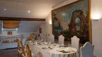 Ein Esszimmer mit einem langen Tisch, der für eine Mahlzeit gedeckt ist, einer weißen Couch im Hintergrund und einem großen Landschaftsbild an der Wand.