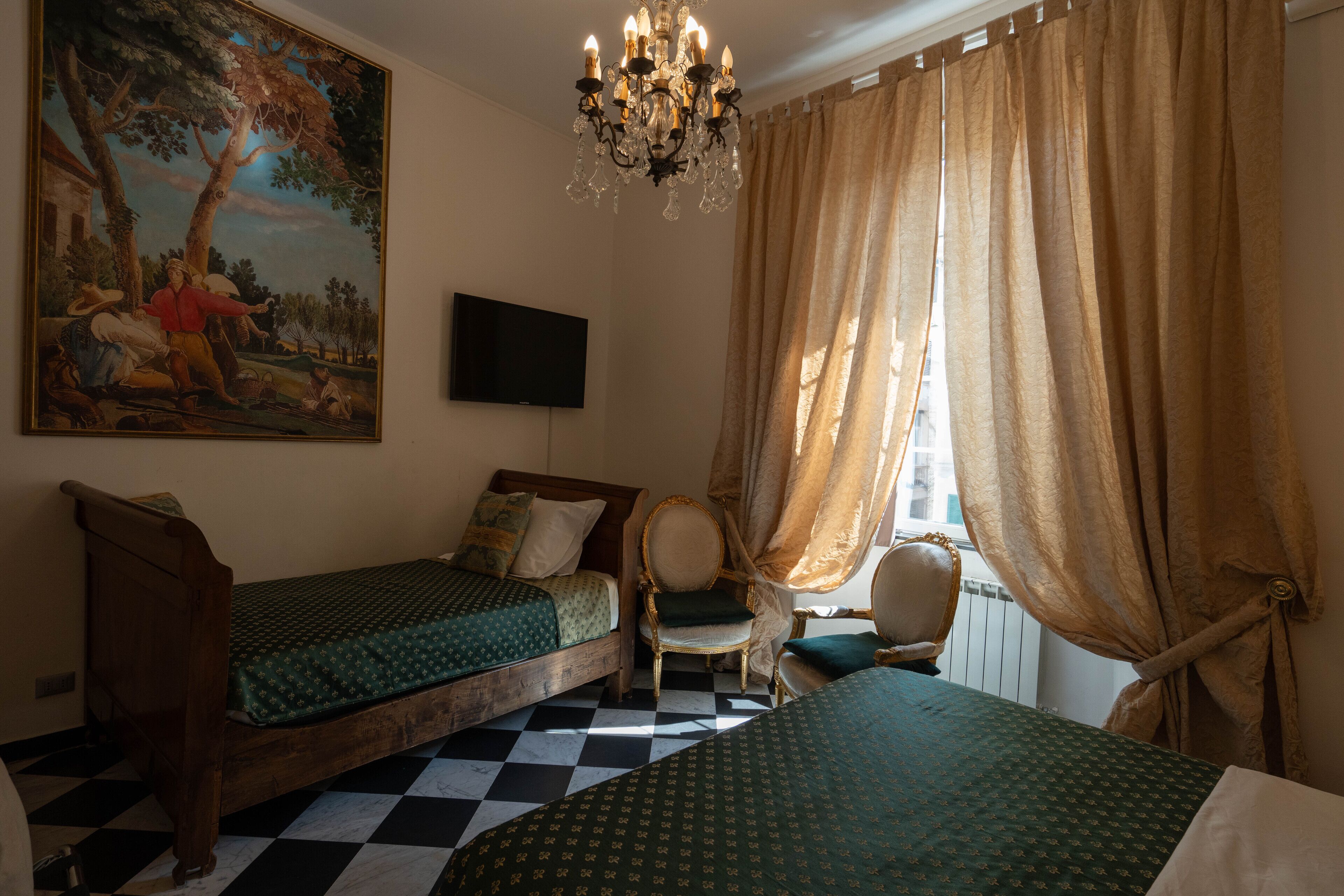 A room with two beds, a chandelier, a painting, a television, and a window with curtains.