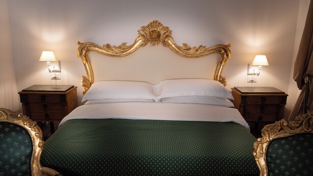 Una cama con cabecera dorada, dos mesitas de noche con lámparas y sillas a juego.