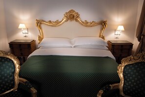 Una cama con cabecera dorada, dos mesitas de noche con lámparas y sillas a juego.