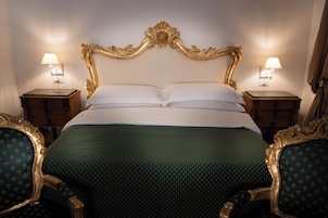 A bed with a gold headboard, two nightstands with lamps, and matching chairs.