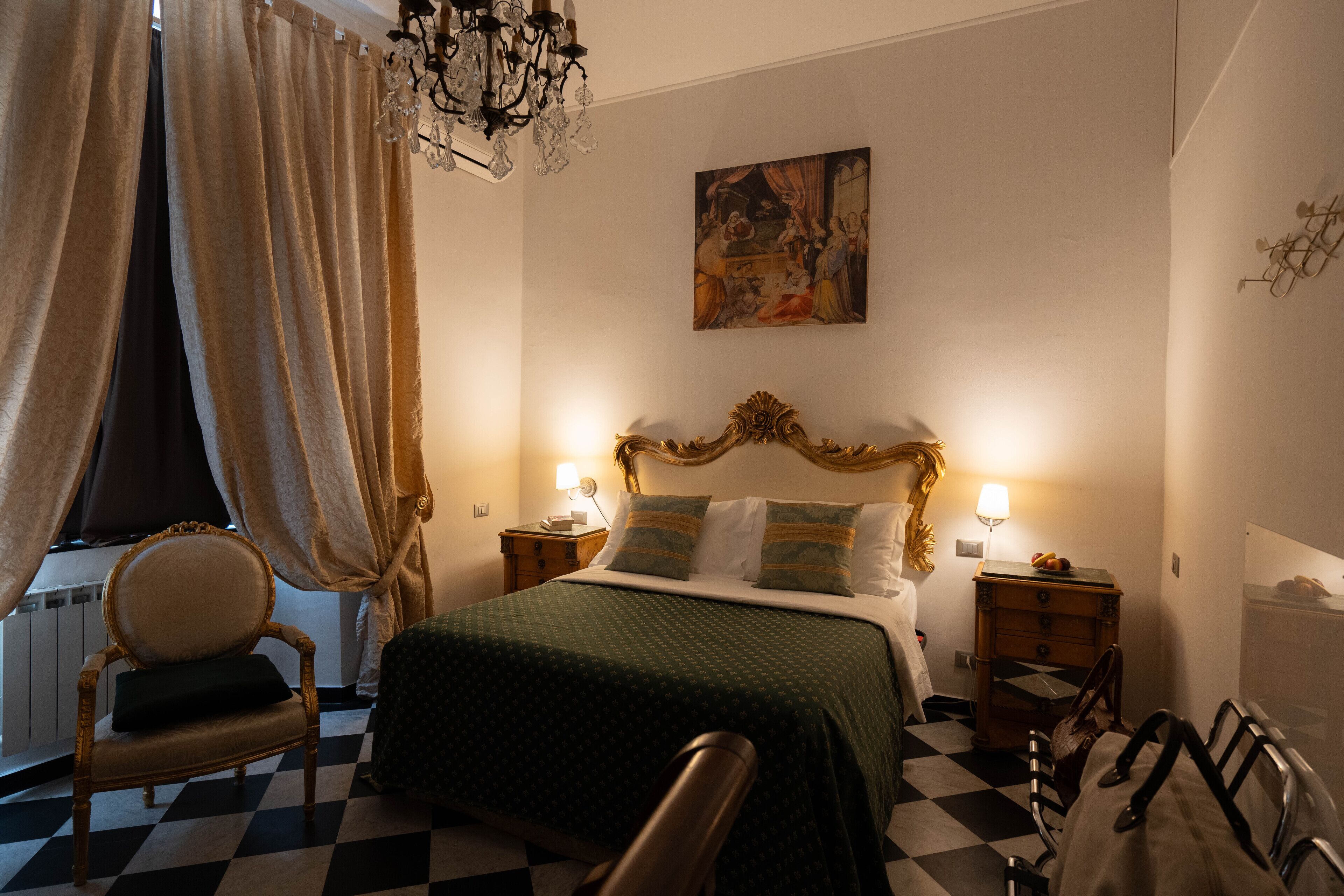 Une chambre d’hôtel avec un sol à carreaux, un lit avec une literie verte, une chaise en bois, un lustre et un tableau accroché au mur.