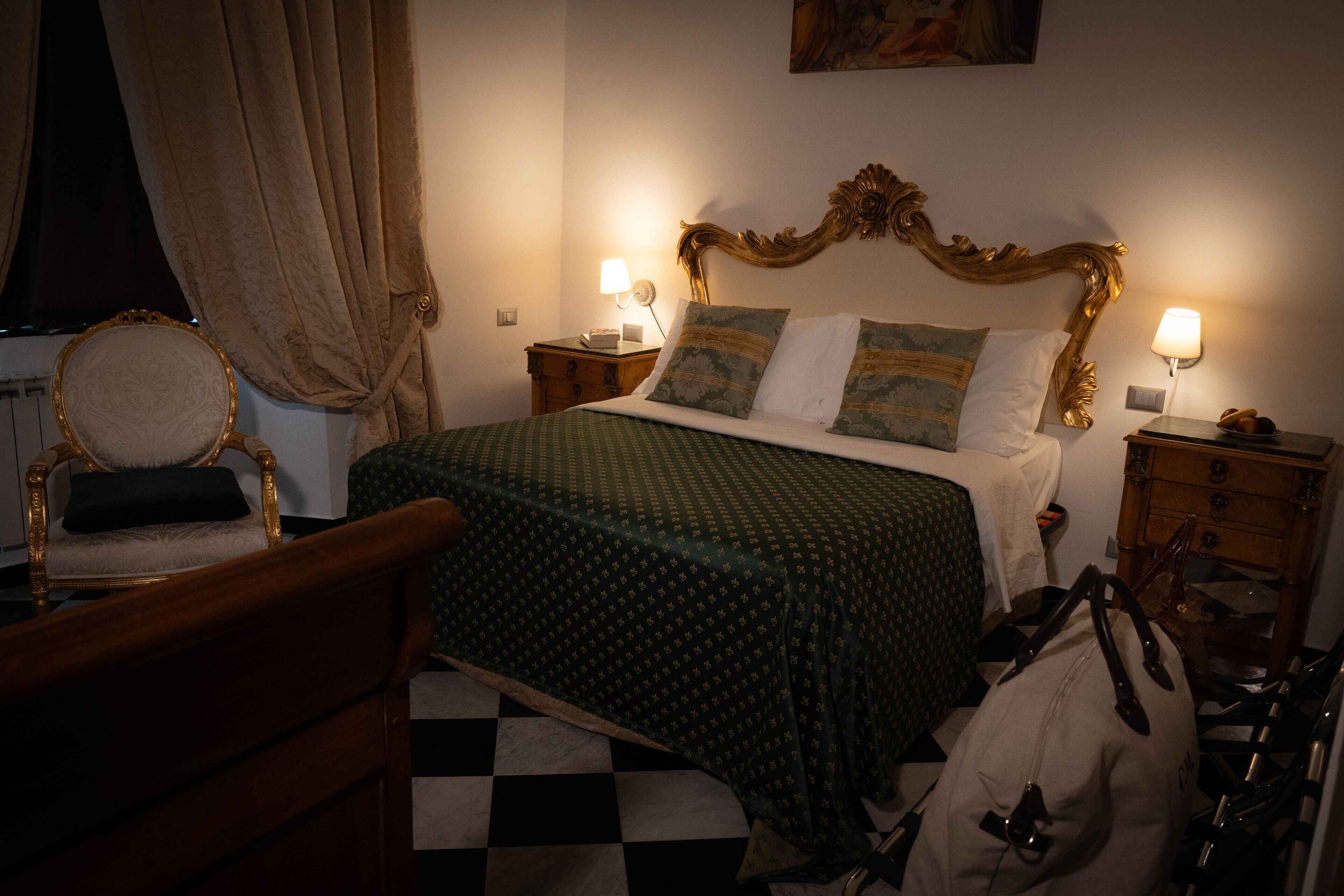 Una habitación de hotel con piso a cuadros, cama con ropa de cama estampada, una silla de madera y una mesita de noche con lámpara.