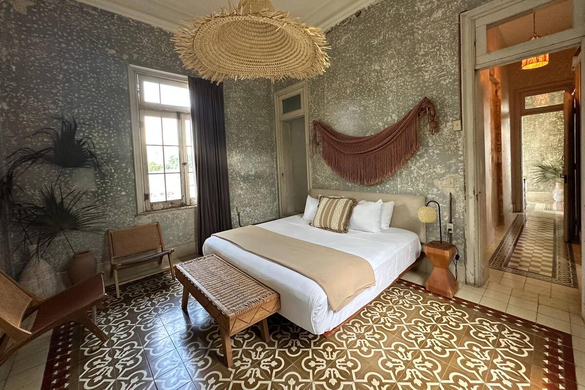 A room with a bed, a woven hanging light fixture, a hammock, a bench, and a patterned floor.
