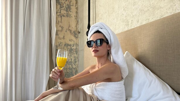 A person sitting on a bed with a towel wrapped around their head, holding a glass of orange juice. - Historic House Hotel Boutique (Mérida)