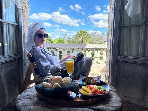 A person sitting on a wooden chair with a tray of food and a drink on a balcony. - Historic House Hotel Boutique (Mérida)