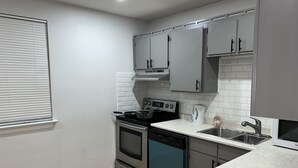 A compact kitchen with white cabinets, a black stove, a dishwasher, and a sink.
