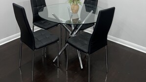 A conference room with a glass table, four black upholstered chairs, a vase with flowers, a clock, and a framed picture on the wall.