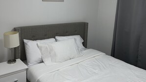 A neatly made bed with white linens, a bedside lamp, and a small bedside table with drawers.