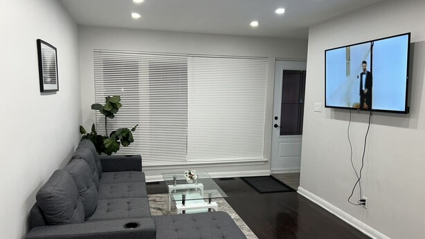 A modern living room with a sectional sofa, a glass coffee table, and a flat-screen TV mounted on the wall.
