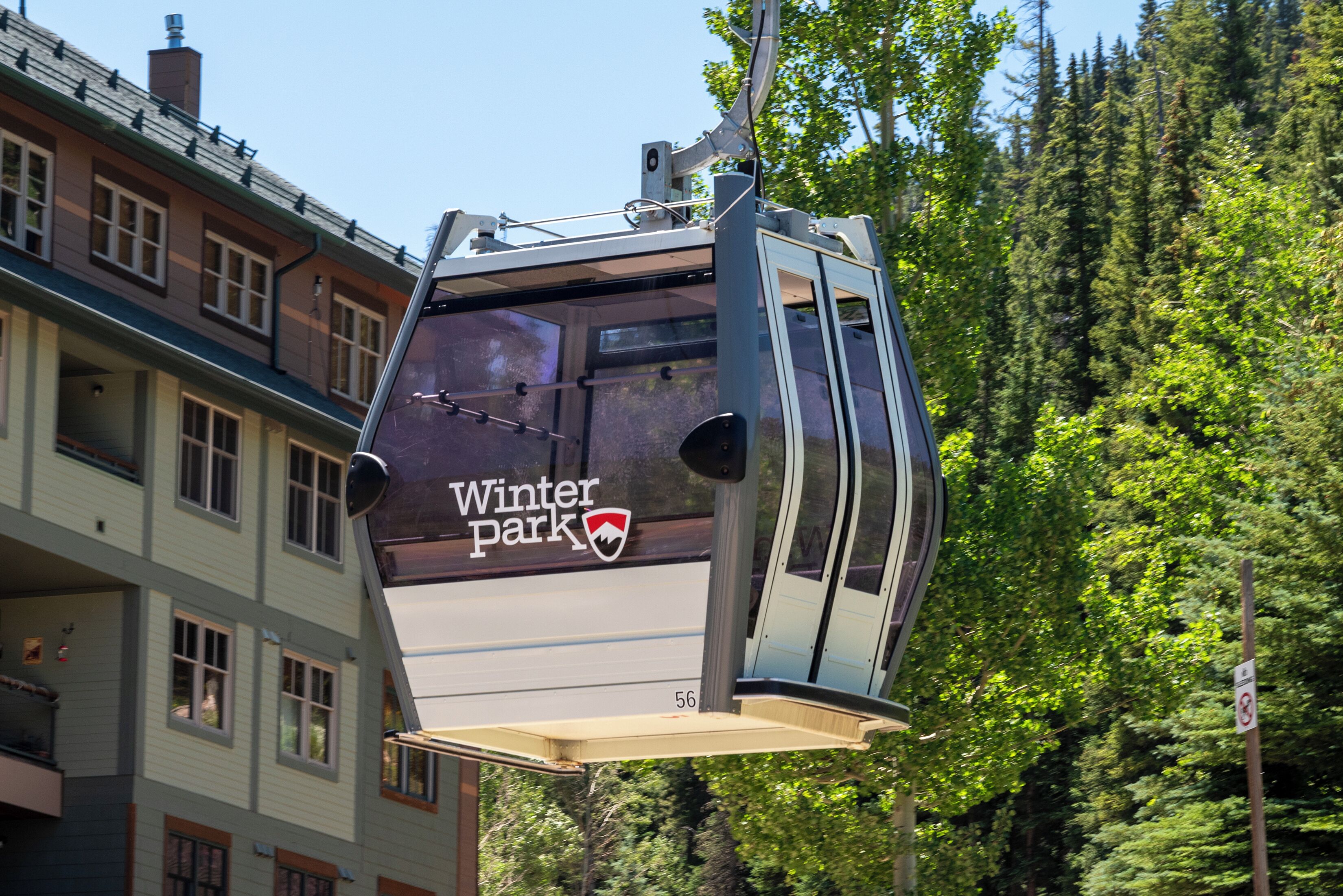 A cable car labeled "Winter Park" suspended above a building with multiple windows and a forested background.