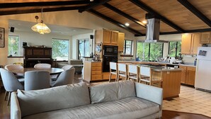 Eine moderne Küche mit Holzausstattung, einer zentralen Kochinsel und einem Essbereich mit einer Couch und Sesseln.