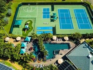 An aerial view of a property with a swimming pool, tennis courts, and a basketball court.