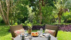 Une table à manger d’extérieur, dressée avec des assiettes, des couverts et des verres, entourée d’une végétation luxuriante et d’arbres.