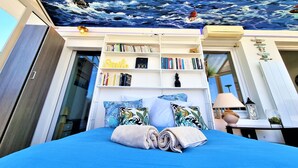 Une chambre avec un grand lit, une bibliothèque remplie de livres, une fresque murale représentant l’océan et un luminaire au plafond.