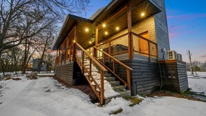 Una cabaña de madera con una escalera que lleva a un porche cubierto, rodeada de nieve.