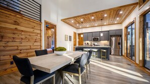 Una cocina moderna con techo de madera, electrodomésticos de acero inoxidable y un comedor con mesa y sillas de madera.