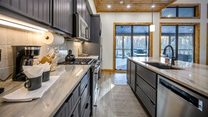 Una cocina moderna con armarios oscuros, electrodomésticos de acero inoxidable y un amplio ventanal con vistas al exterior.