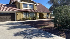 A two-story house with a brown tiled roof, a garage, and a front yard with a tree and shrubs. - Private Two Bedroom, Two TVs, One Bathroom Casita! (Las Vegas)