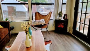 A room with a wooden table, a brown leather chair, a small rug, and a window with a view of a building outside.