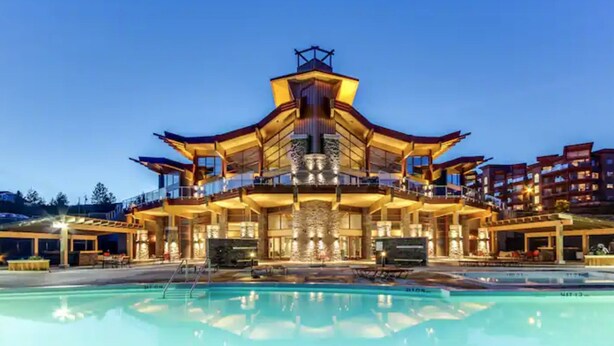 Un edifici gran de diversos pisos amb un atrium central i balcons, envoltat d'una piscina.