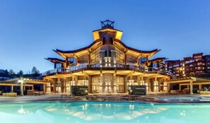 A large, multi-story building with a central atrium and balconies, surrounded by a swimming pool. - Beautiful Lake, Pool and Mountain Views (West Kelowna)