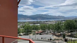 Vista des d'un balcó sobre una vila amb muntanyes al fons, un llac i una combinació d'edificis residencials i comercials.