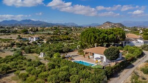 Una villa con piscina, rodeada de exuberante vegetación y montañas al fondo.