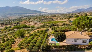 Una villa con piscina, rodeada de olivares y con montañas al fondo.
