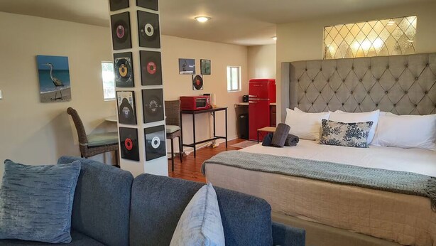 Ein Schlafzimmer mit einem gro ßen Bett, einem grauen Polstersofa, einem Esstisch mit einer roten Mikrowelle und einer Wand, die mit Schallplatten dekoriert ist.
