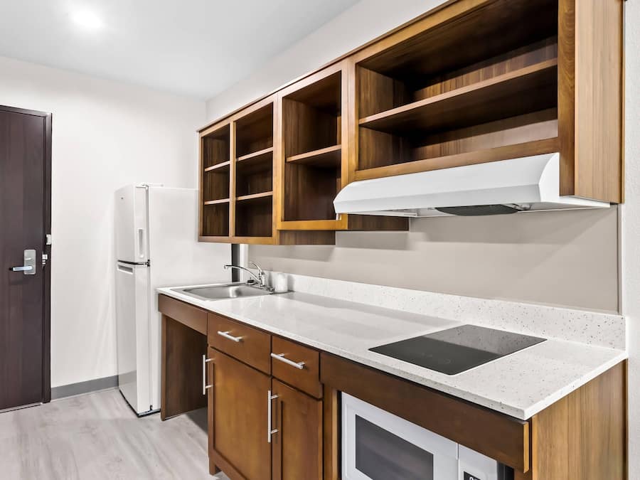 A compact kitchen with a refrigerator, a sink, and wooden cabinets.