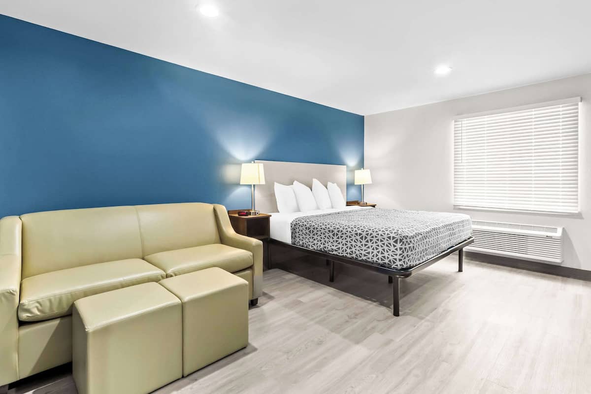 Una habitación de hotel moderna con cama, sofá, mesita de noche y ventana con persianas.
