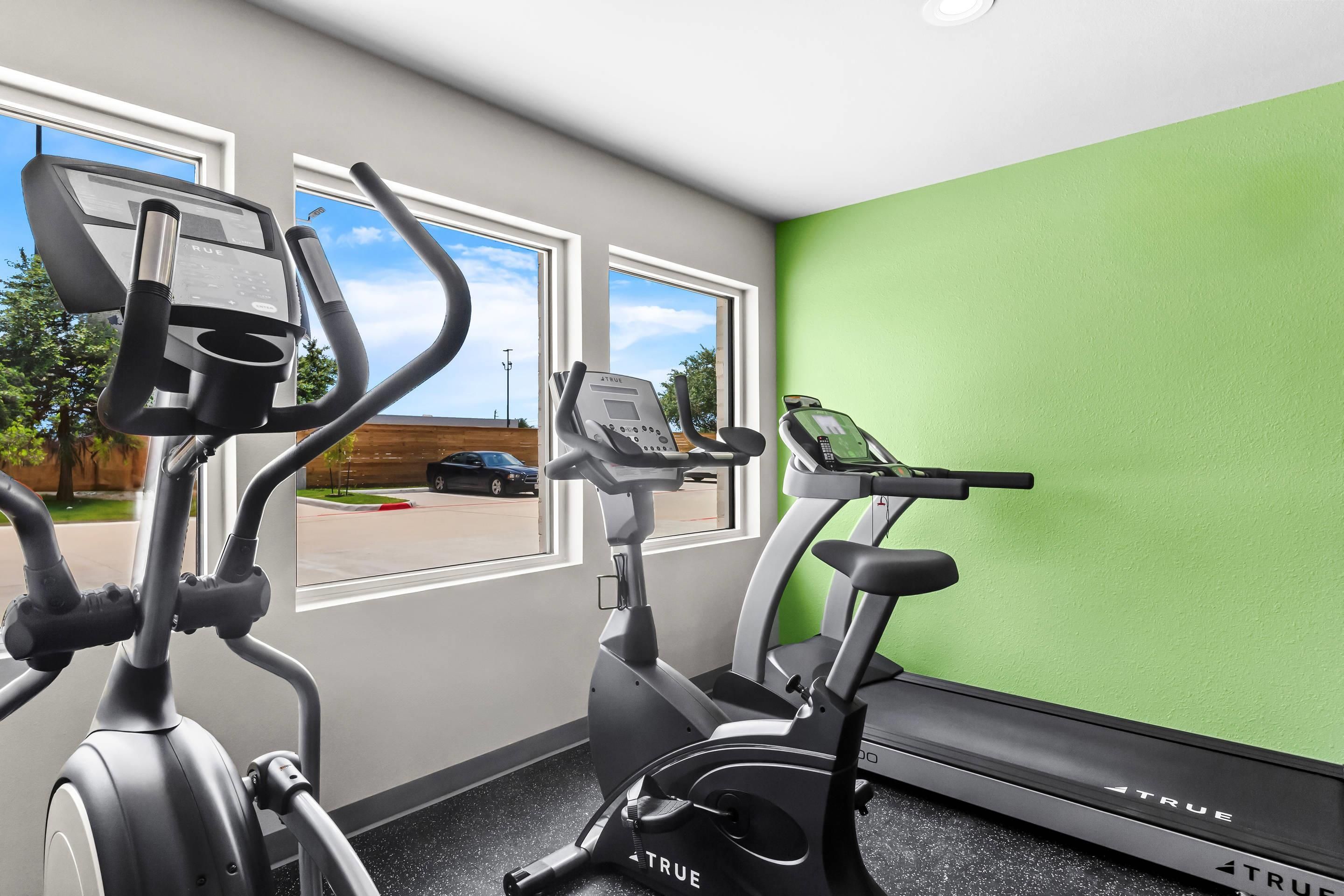 Une salle de sport équipée de deux vélos d’exercice et d’un tapis de course, dotée de grandes fenêtres et d’un mur végétal.