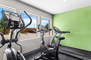 A gym with two exercise bikes and a treadmill, large windows, and a green wall. - Woodspring Suites South Houston Hobby (Houston)