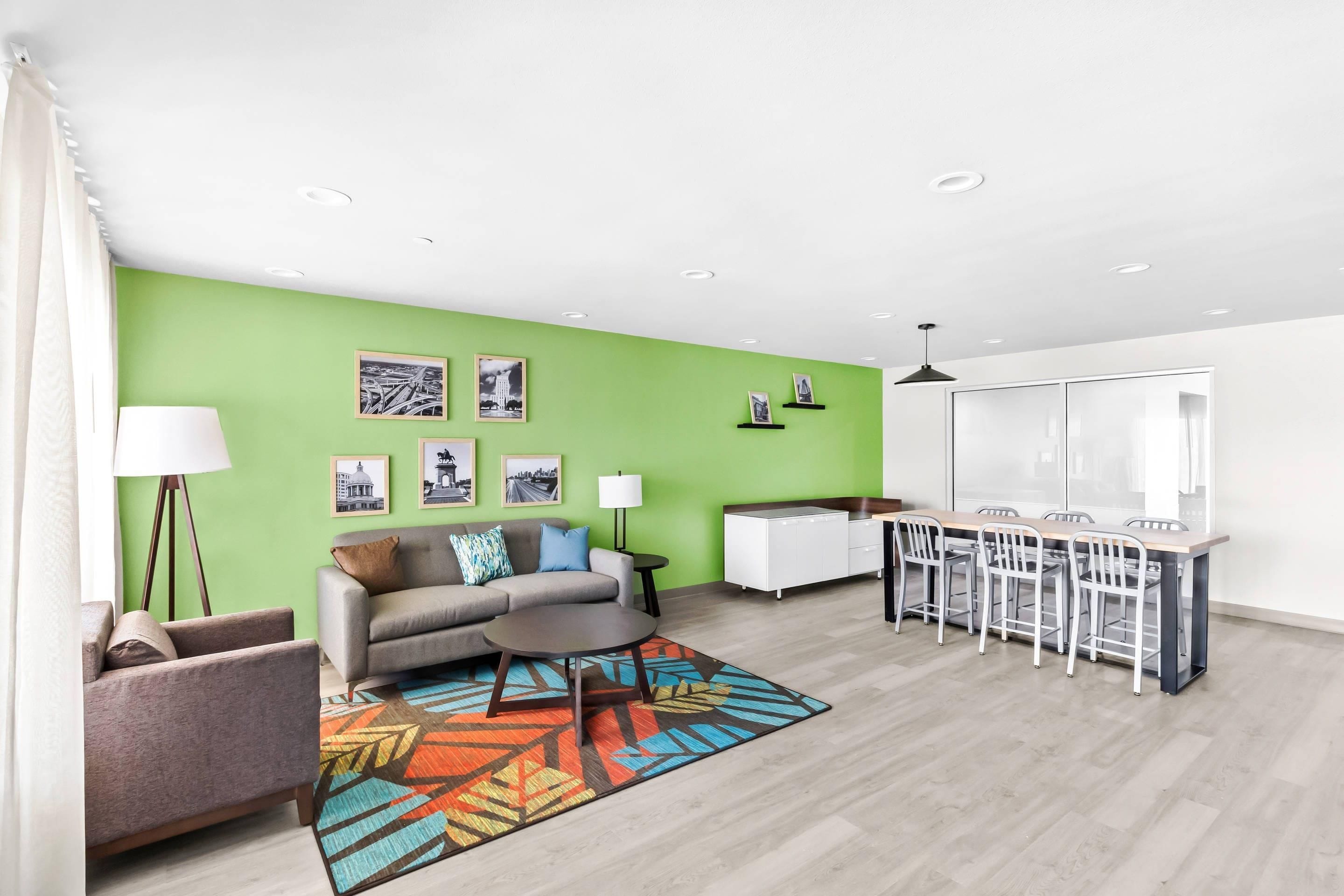 A modern living room with a green accent wall, a sofa, a coffee table, and a dining area with a white table and chairs.