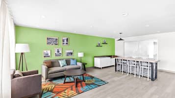 A modern living room with a green accent wall, a sofa, a coffee table, and a dining area with a white table and chairs.