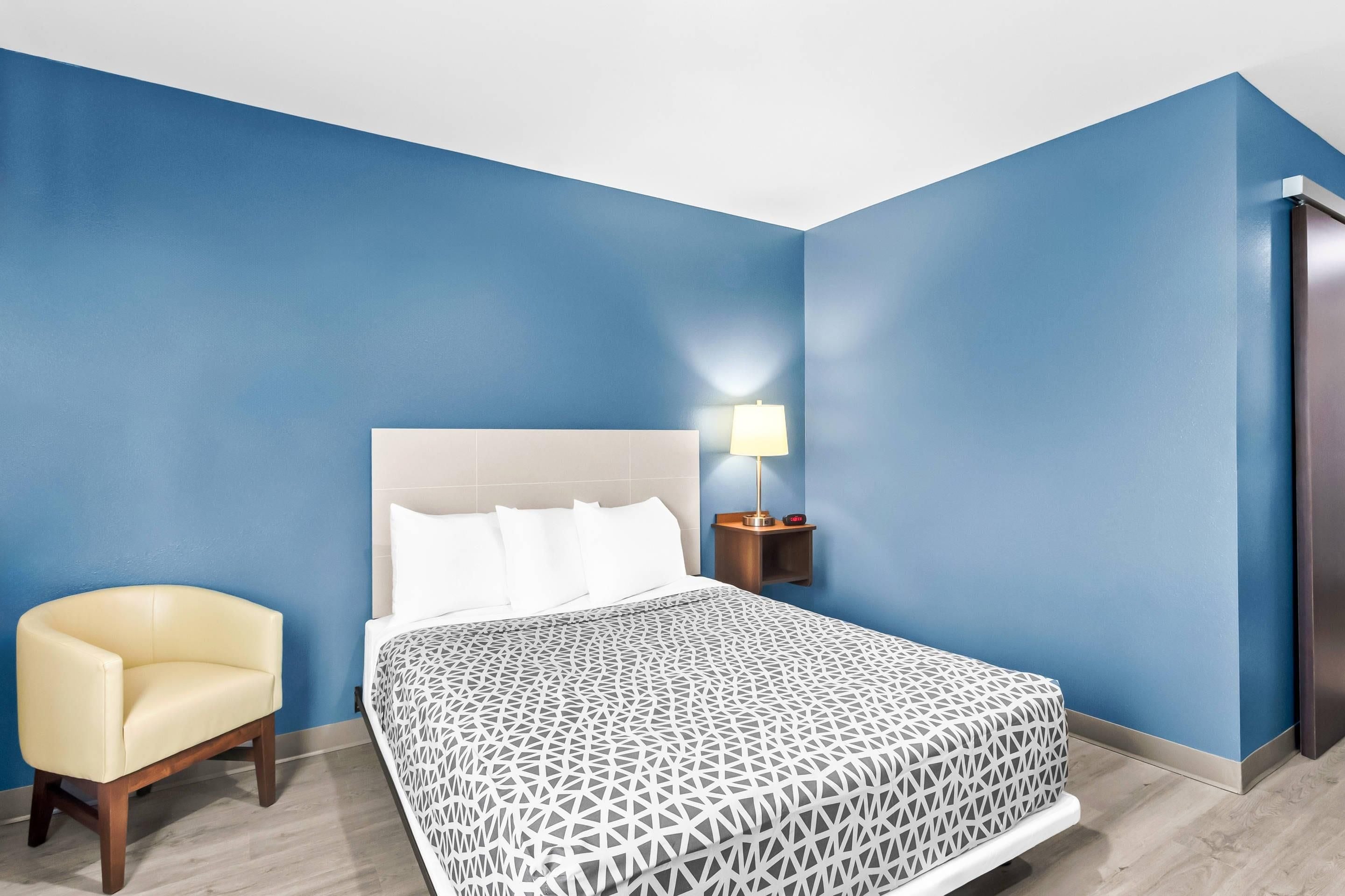 A hotel room with a bed, a bedside table with a lamp, a chair, and a wardrobe.
