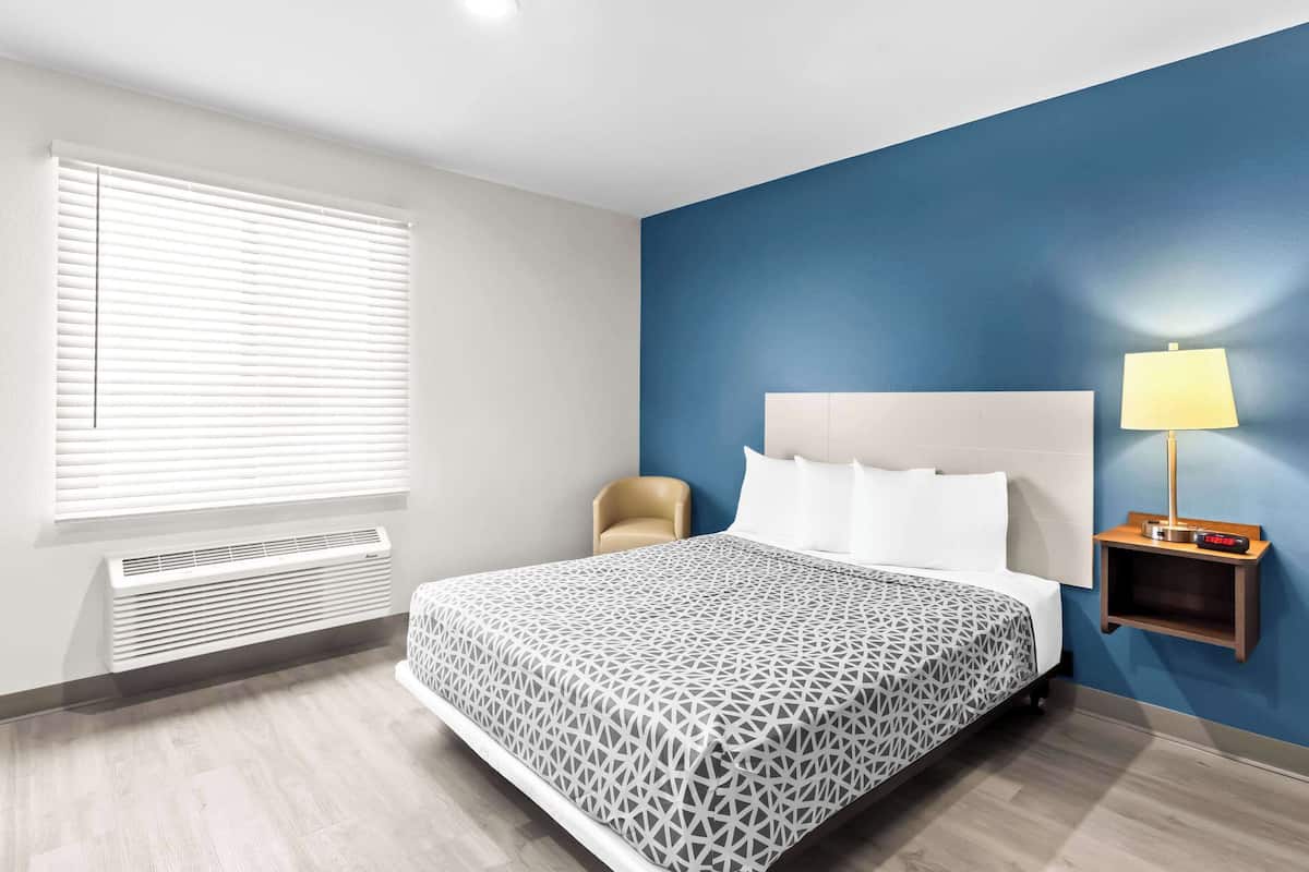 Habitación de hotel con cama, una silla, mesita de noche con lámpara y un calentador de pared.