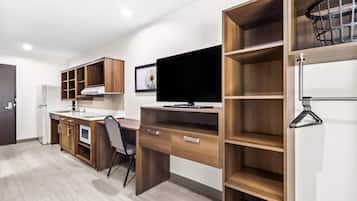 A modern kitchen with wooden cabinets, a built-in oven, and a large flat-screen TV.