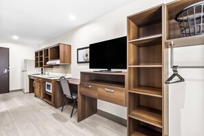 A modern kitchen with wooden cabinets, a built-in oven, and a large flat-screen TV. - Woodspring Suites South Houston Hobby (Houston)