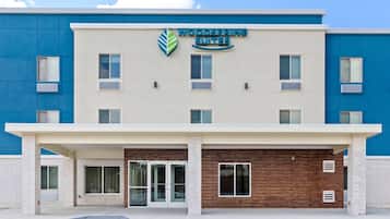 Un edificio con un letrero de Woodspring Suites, con fachada plana y múltiples ventanales, y un acceso cubierto.