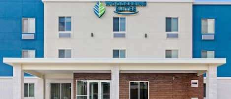 A building with a sign for Woodspring Suites, featuring a flat facade with multiple windows and a covered entrance.