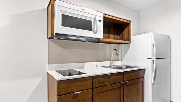 A compact kitchen with a microwave, double sink, and a refrigerator. - Woodspring Suites South Houston Hobby (Houston)