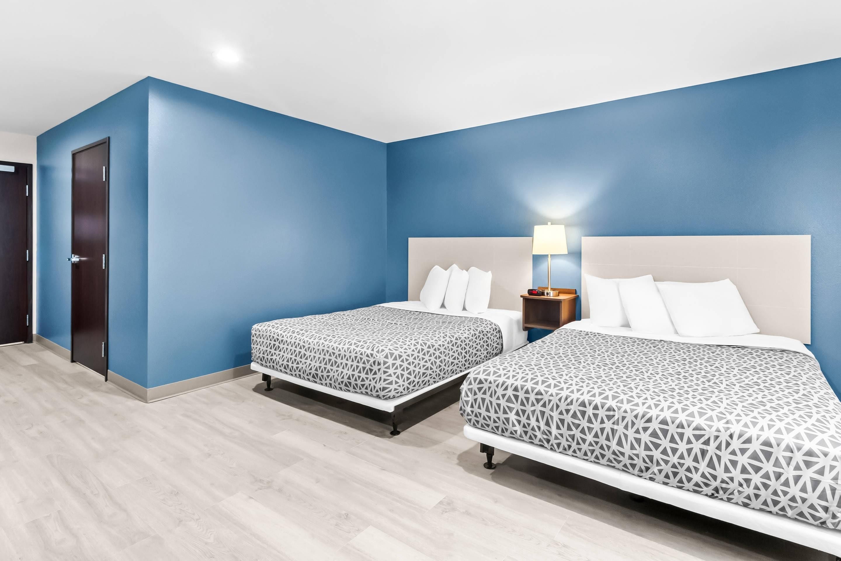 Ein Hotelzimmer mit zwei Betten, einer Tür und einem Nachttisch mit Lampe.