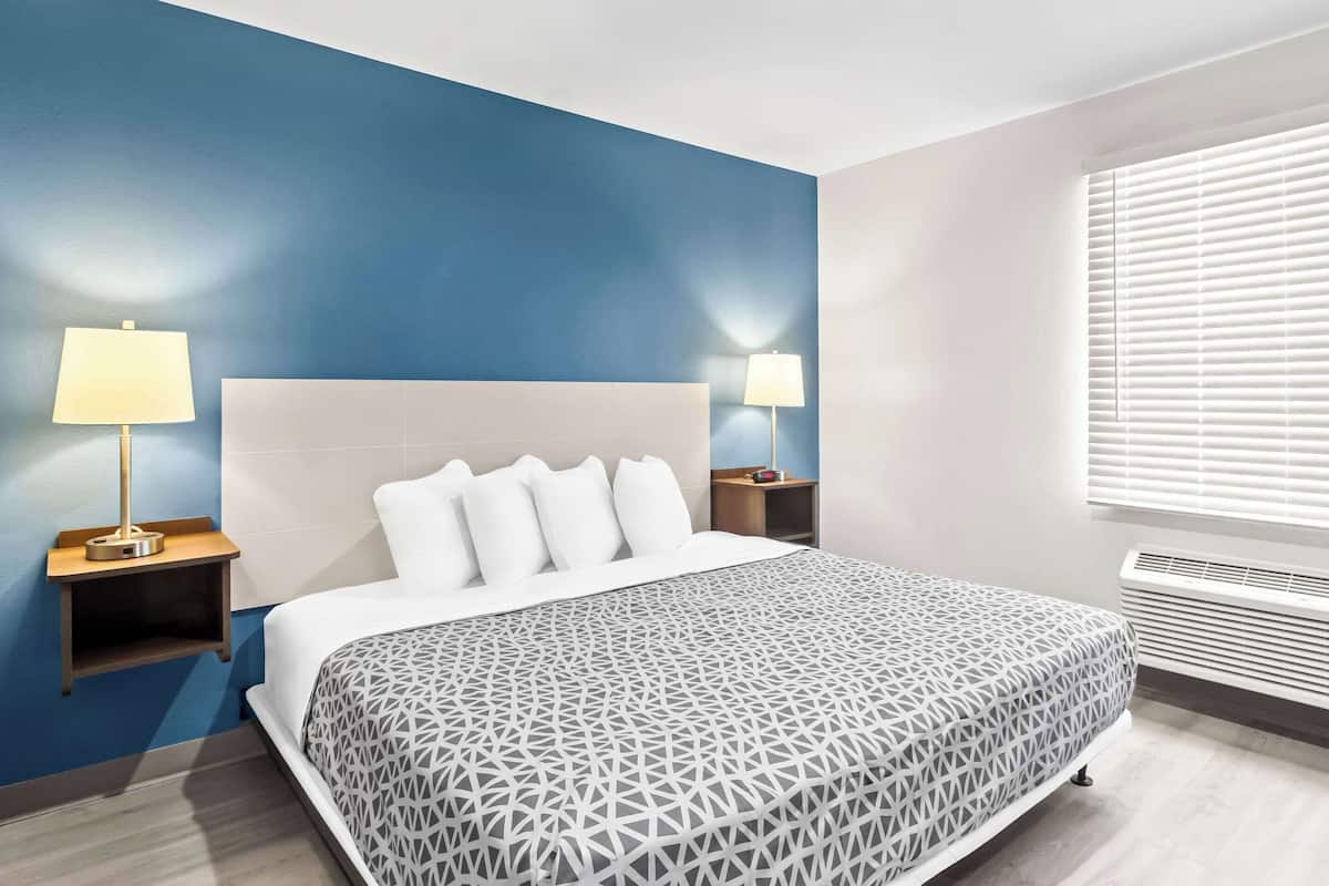 Habitación de hotel moderna con una cama grande, dos mesitas de noche con lámparas, una ventana con persianas y un calentador incorporado.