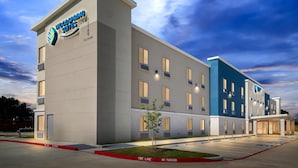 A hotel with a modern design, featuring a prominent logo on the facade, multiple windows, and a parking area with marked spaces. - Woodspring Suites South Houston Hobby (Houston)