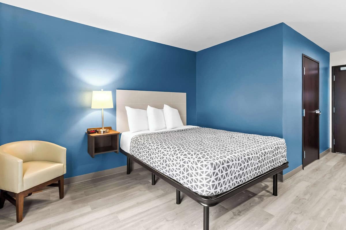 Habitación de hotel con cama, mesita de noche, una silla y una puerta.