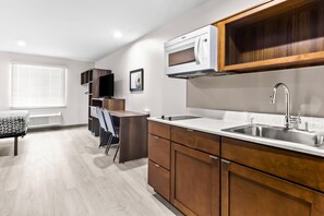 A modern kitchen with a built-in microwave, stainless steel sink, and wooden cabinets. - Woodspring Suites South Houston Hobby (Houston)