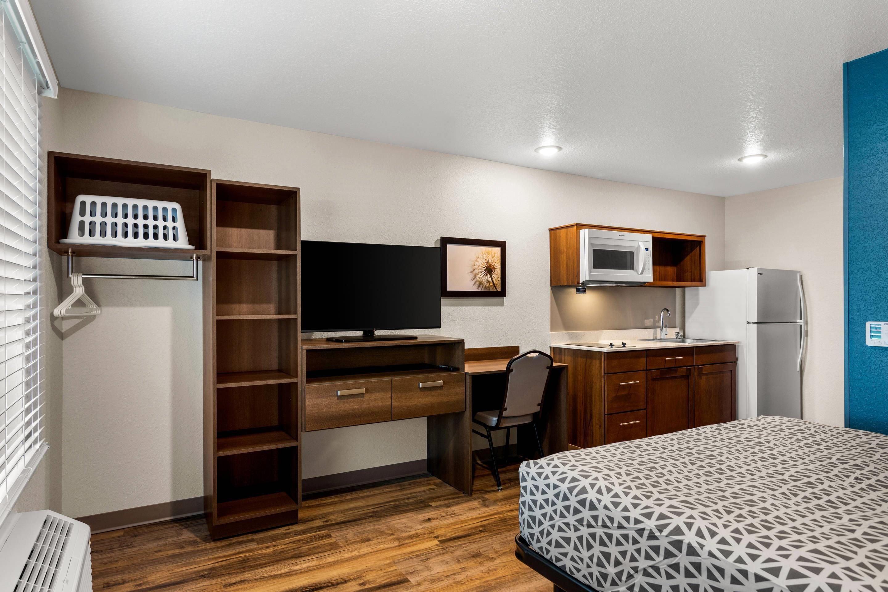 A compact room with a bed, a desk with a computer, a microwave, and a refrigerator.