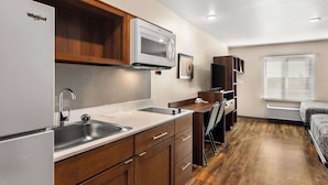 Una cocina compacta con un refrigerador Whirlpool, un microondas y un lavamanos. Hay un pequeño comedor con una silla y una mesa.